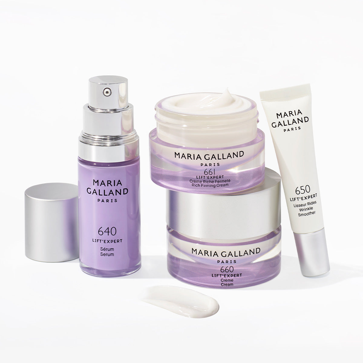 Vier Hautpflegeprodukte von Maria Galland Paris in violetter und weißer Verpackung, darunter ein Serum, zwei Cremetiegel und eine Tube Augenglätter mit Creme auf weißer Fläche.