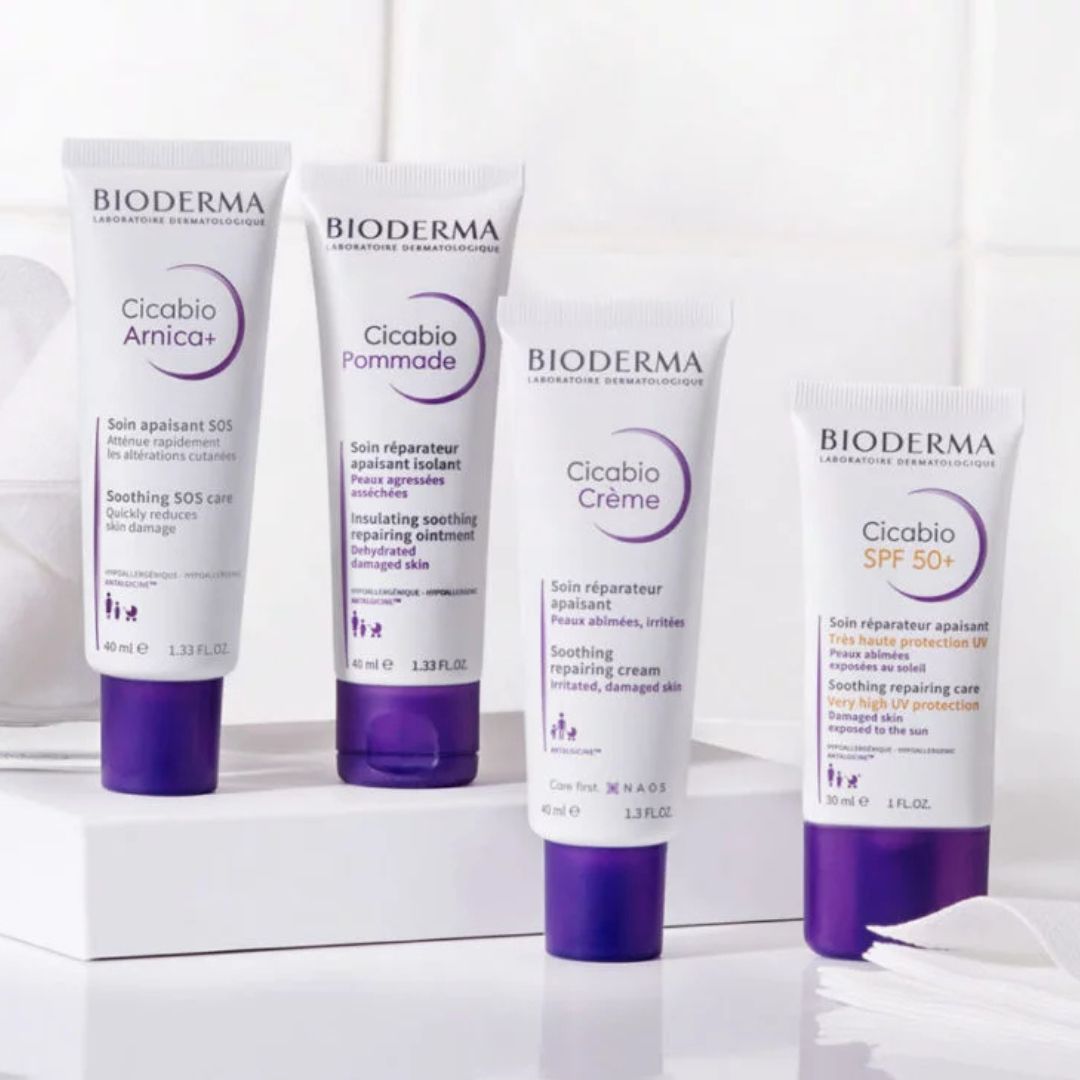Vier Bioderma-Hautpflegeprodukte mit lila-weißer Verpackung werden auf einer weißen Fläche präsentiert, darunter Cicabio Arnica+, Cicabio Pommade, Cicabio Crème und Cicabio SPF 50+.