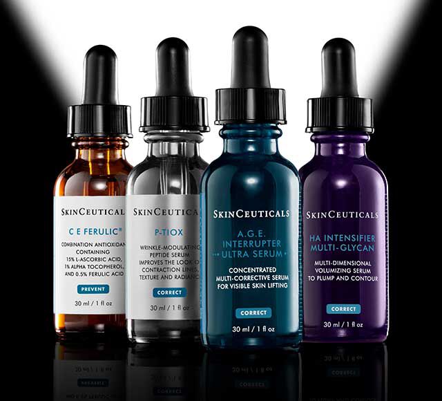 Vier SkinCeuticals-Serumflaschen mit Tropfer sind nebeneinander vor einem schwarzen Hintergrund angeordnet, hinter dem das Licht die farbigen Etiketten und Glasflaschen hervorhebt.