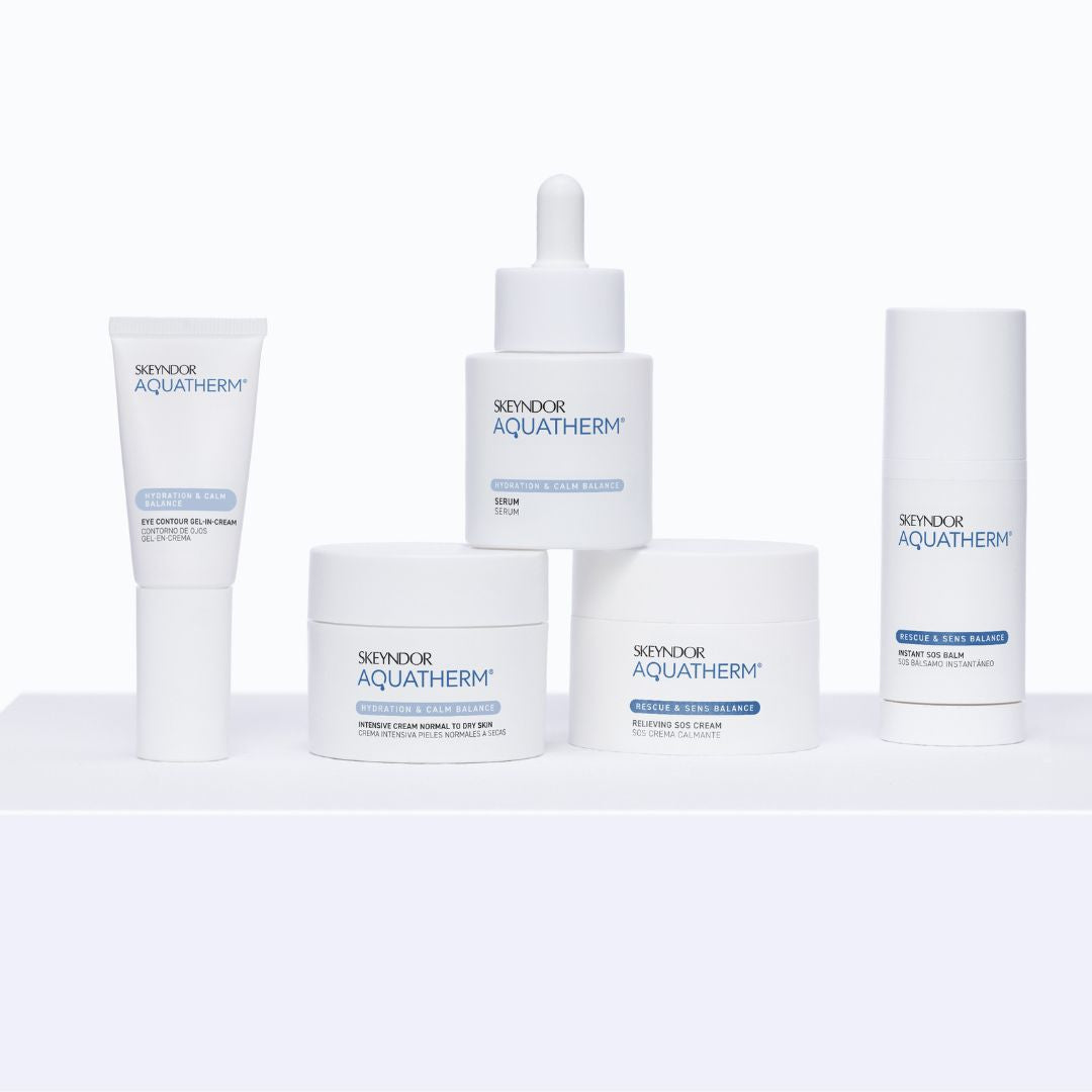 Fünf weiße Hautpflegeprodukte aus der Aquatherm-Linie von Skeyndor sind übersichtlich auf einer weißen Fläche mit einfarbigem Hintergrund angeordnet. Zu den Produkten gehören Cremes, Serum und Augenkonturcreme.