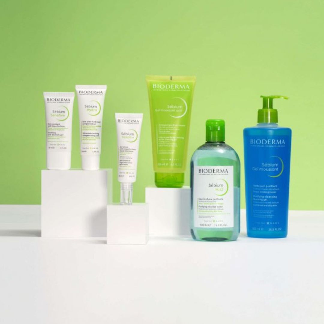 Eine Kollektion von Bioderma Sébium Hautpflegeprodukten, einschließlich Cremes, Reinigungsmittel, Toner und Gel, die auf weißen Blöcken vor einem grünen und weißen Hintergrund präsentiert werden.
