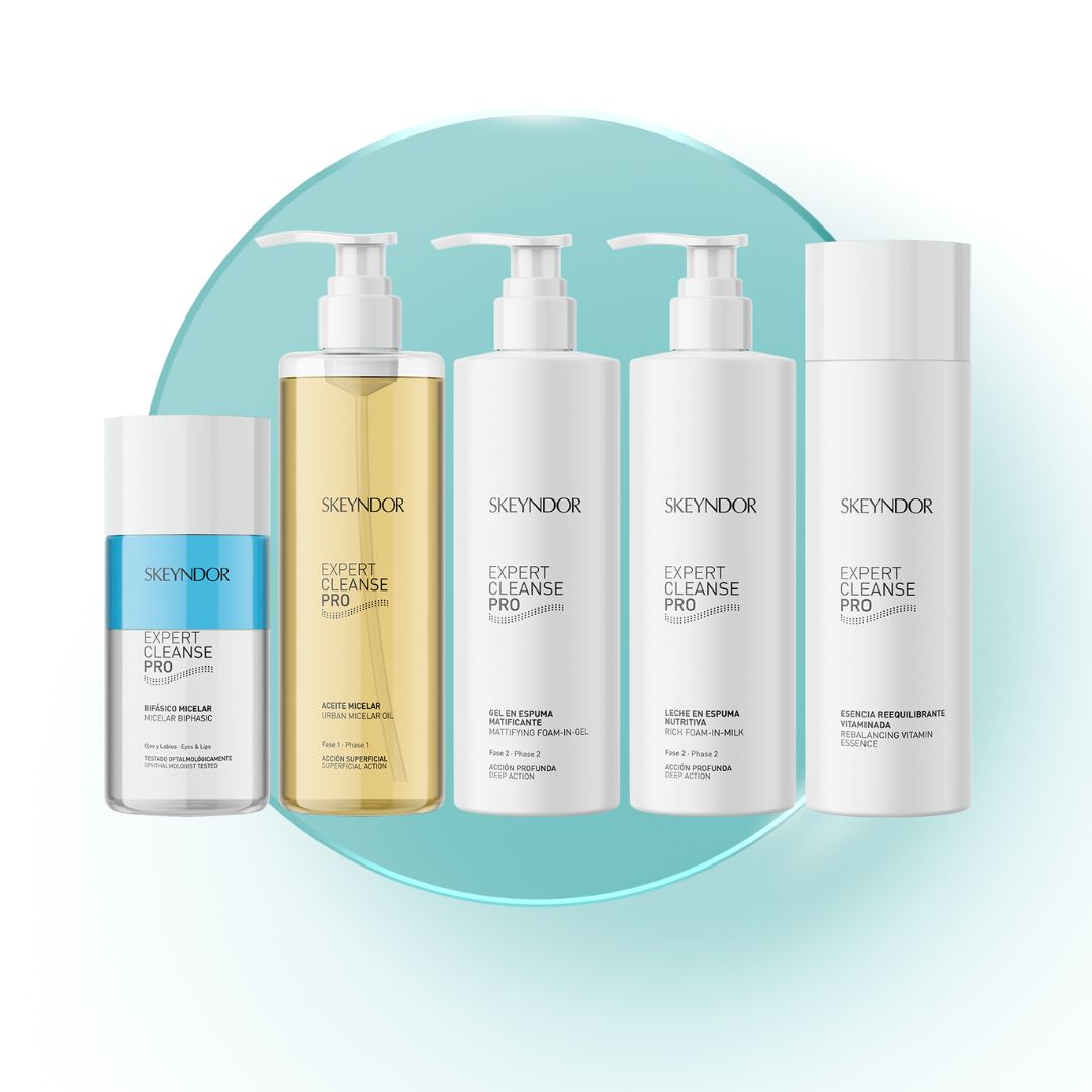 Fünf Skeyndor Expert Cleanse Pro Hautpflegeflaschen sind in einer Reihe auf einem hellblauen, runden Hintergrund angeordnet, darunter Mizellenwasser, Öl, Gel, Lotion und Peeling.