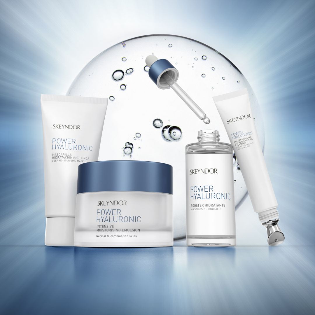 Eine Kollektion von Skeyndor Power Hyaluronic Hautpflegeprodukten, einschließlich Creme, Serum und Maske, angeordnet vor einem blauen, strahlenden Hintergrund mit einem Tropfer und Wassertropfen.
