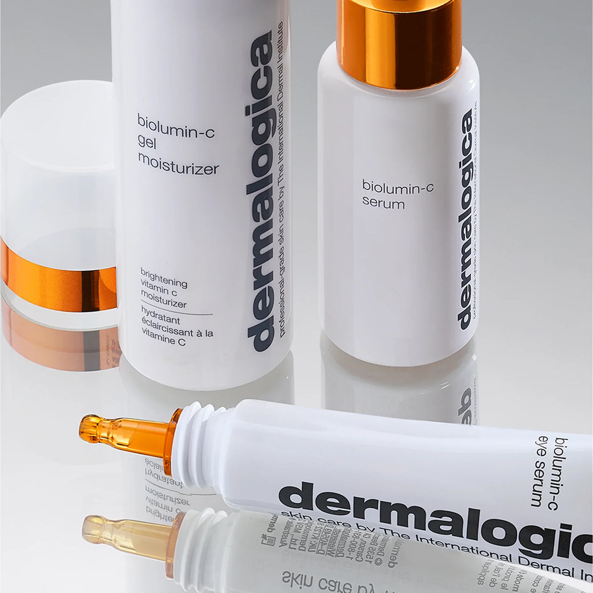 Drei Dermalogica-Hautpflegeprodukte - Biolumin-C-Gel-Feuchtigkeitscreme, Serum und Augenserum - sind auf einer spiegelnden Oberfläche angeordnet und zeigen weiße Behälter mit einfachem, modernem Text und orangefarbenen Akzenten.