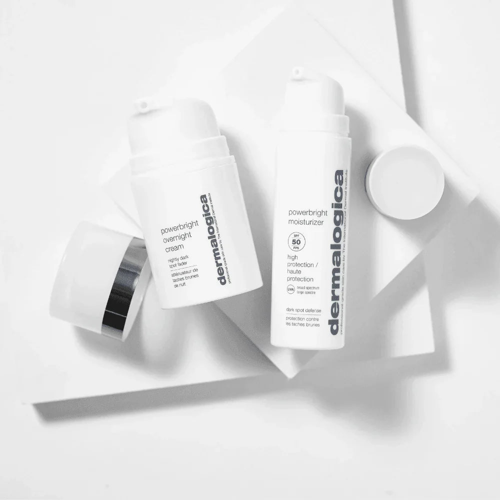 Zwei Dermalogica PowerBright-Pflegeflaschen und ein offener Tiegel mit weißem Deckel sind auf einer weißen geometrischen Fläche in einem minimalistischen, kontrastreichen Stil angeordnet.