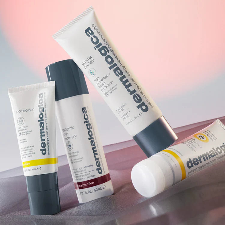 Vier Dermalogica-Pflegeprodukte in Tuben und Flaschen sind auf einer rosafarbenen und lilafarbenen Fläche angeordnet, wobei ein weicher, verschwommener Hintergrund und eine subtile Beleuchtung die Verpackungen hervorheben.