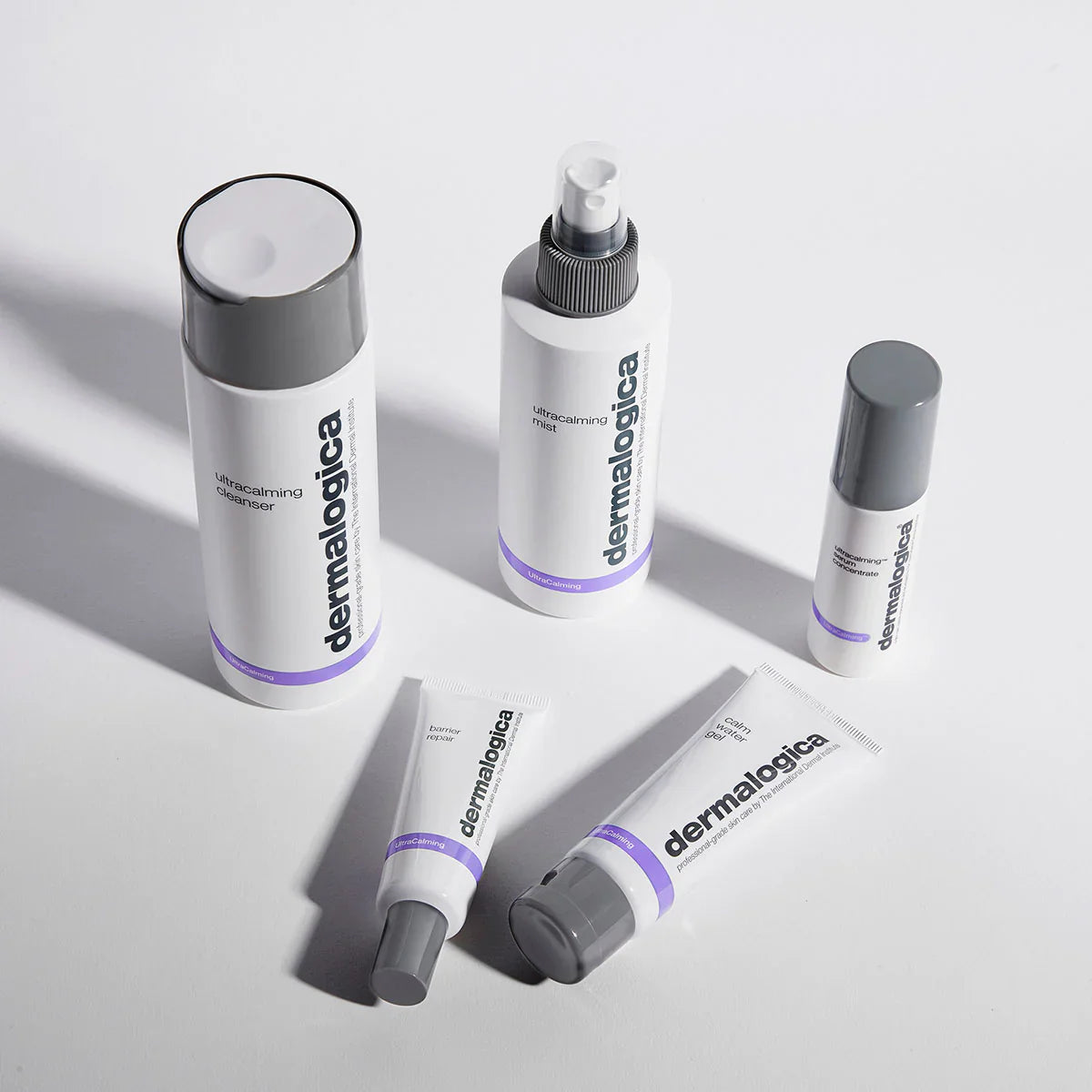Fünf Dermalogica-Hautpflegeprodukte auf einer weißen Fläche, darunter Flaschen, ein Spray und Tuben mit weißer Verpackung, grauen Kappen und violetten Akzenten, alle ästhetisch angeordnet.