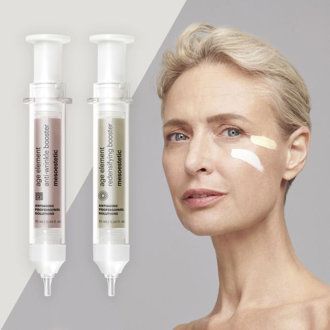 Eine reife Frau mit kurzen blonden Haaren und zwei Cremetupfern auf der Wange steht neben zwei spritzenförmigen Hautpflegeproduktflaschen mit der Aufschrift age element anti-wrinkle booster und redensifying booster.