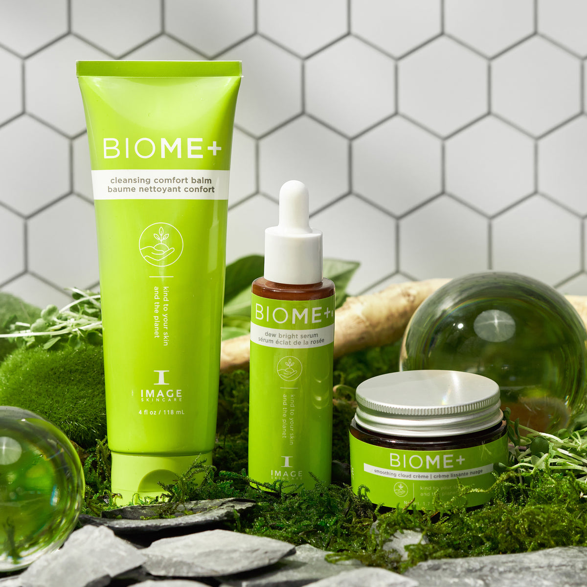 Drei grüne BIOME+ Hautpflegeprodukte werden auf Moos mit Glaskugeln, Steinen und einem weißen sechseckigen Fliesenhintergrund ausgestellt, wodurch eine frische, natürliche und moderne Spa-ähnliche Szene entsteht.