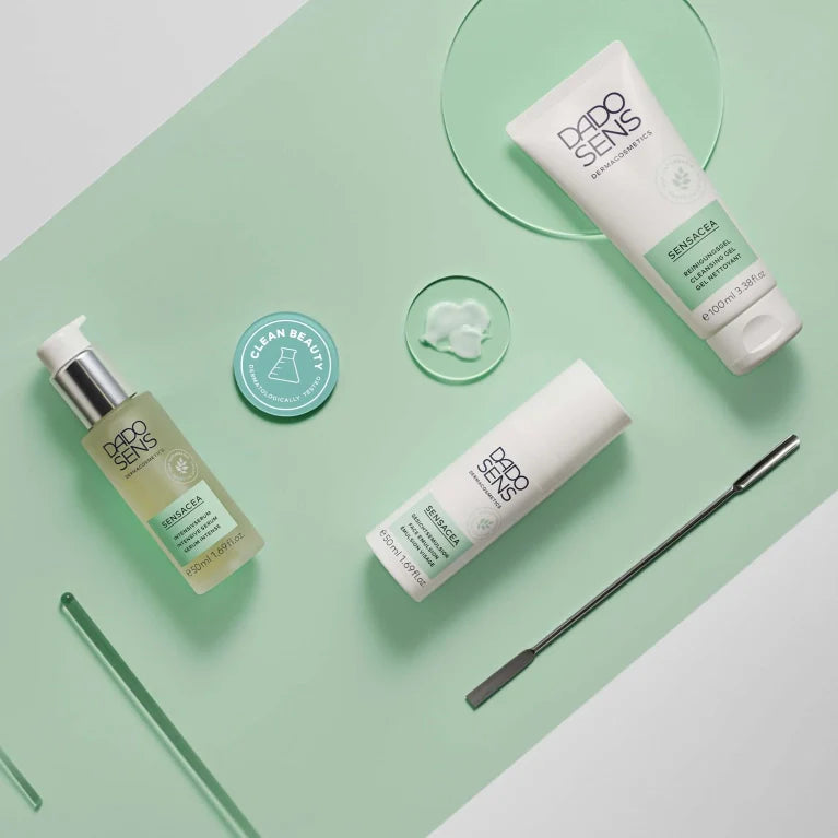 Drei DADO SENS-Hautpflegeprodukte auf einem mintgrünen Hintergrund mit einer "Clean Beauty"-Plakette, einem Spatel und einem durchsichtigen Cremetupfer; die Produkte sind übersichtlich in einem flachen Layout angeordnet.