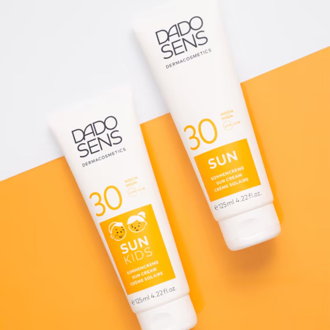 Zwei weiße Tuben Dado Sens Sonnenschutzmittel SPF 30 auf weißem und orangefarbenem Hintergrund; eine mit der Aufschrift "Sun Kids" und Tiersymbolen, die andere mit der Aufschrift "Sun.".