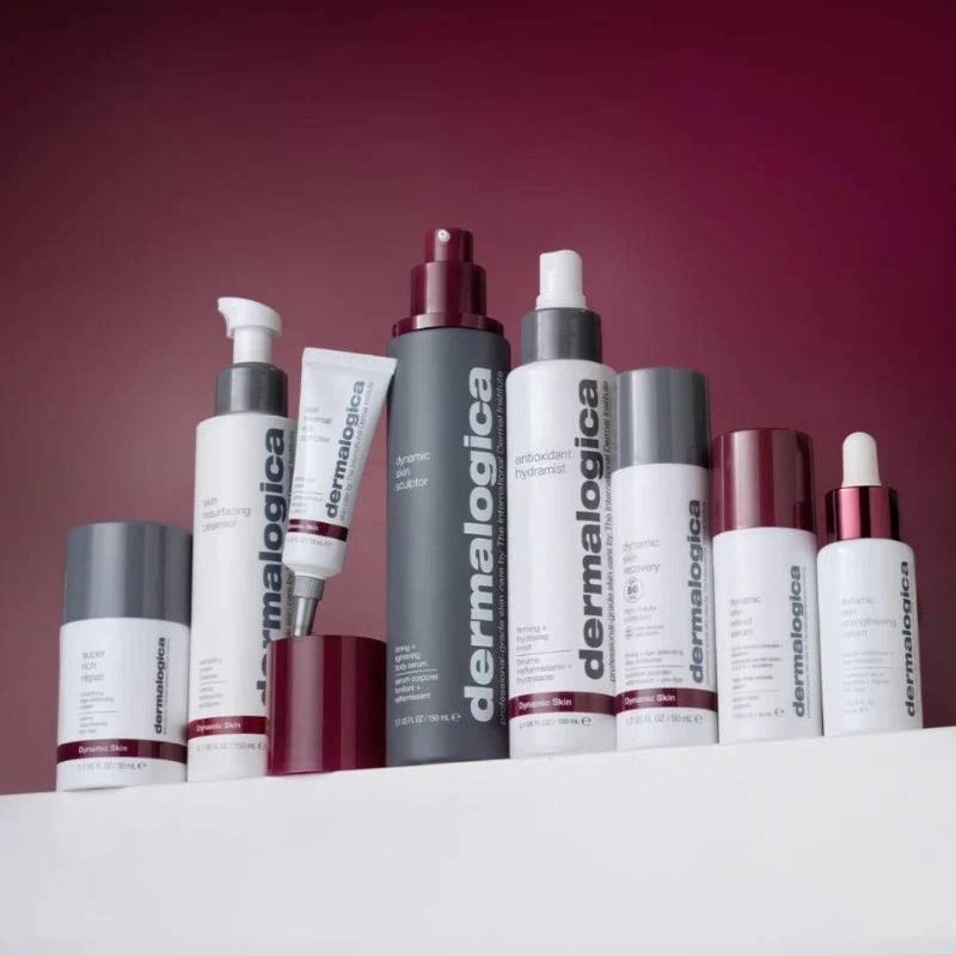 Eine Reihe von sieben Dermalogica-Hautpflegeprodukten, darunter Mists, Cleanser, Moisturizer und Cremes, aufrecht angeordnet auf einer weißen, reflektierenden Oberfläche.