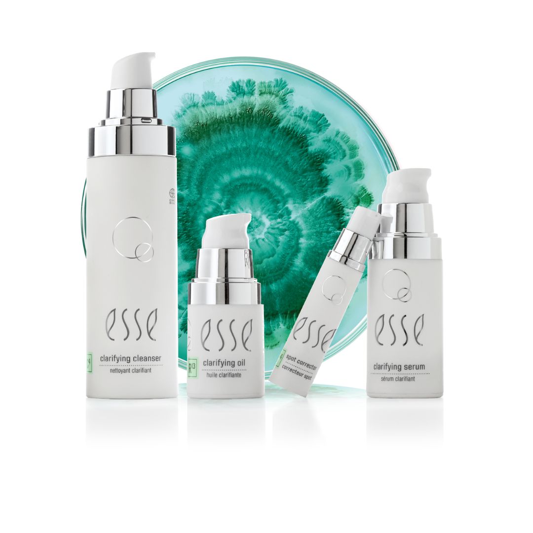 Vier weiße Flaschen mit Hautpflegeprodukten von Esse stehen vor einem grün-weißen kreisförmigen Design, darunter ein klärender Reiniger, ein Öl und ein Serum, jeweils mit silbernen Pumpaufsätzen auf weißem Hintergrund.