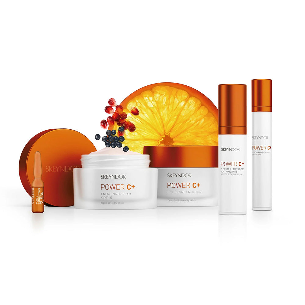 Eine Kollektion von Skeyndor Power C+ Hautpflegeprodukten wird vor einer Orangenscheibe und Beeren gezeigt, mit weißer und oranger Verpackung auf weißem Hintergrund.