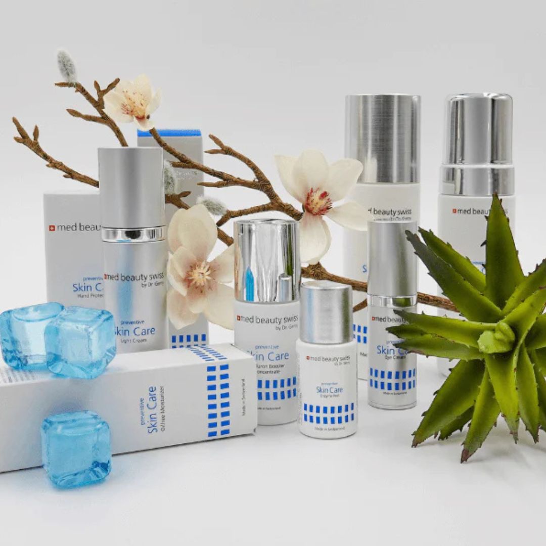 Ein Display mit Hautpflegeprodukten mit silbernen Kappen, weißen und blauen Verpackungen, umgeben von Magnolienblüten, grünen Sukkulenten und blauen Eiswürfeln auf weißem Hintergrund.