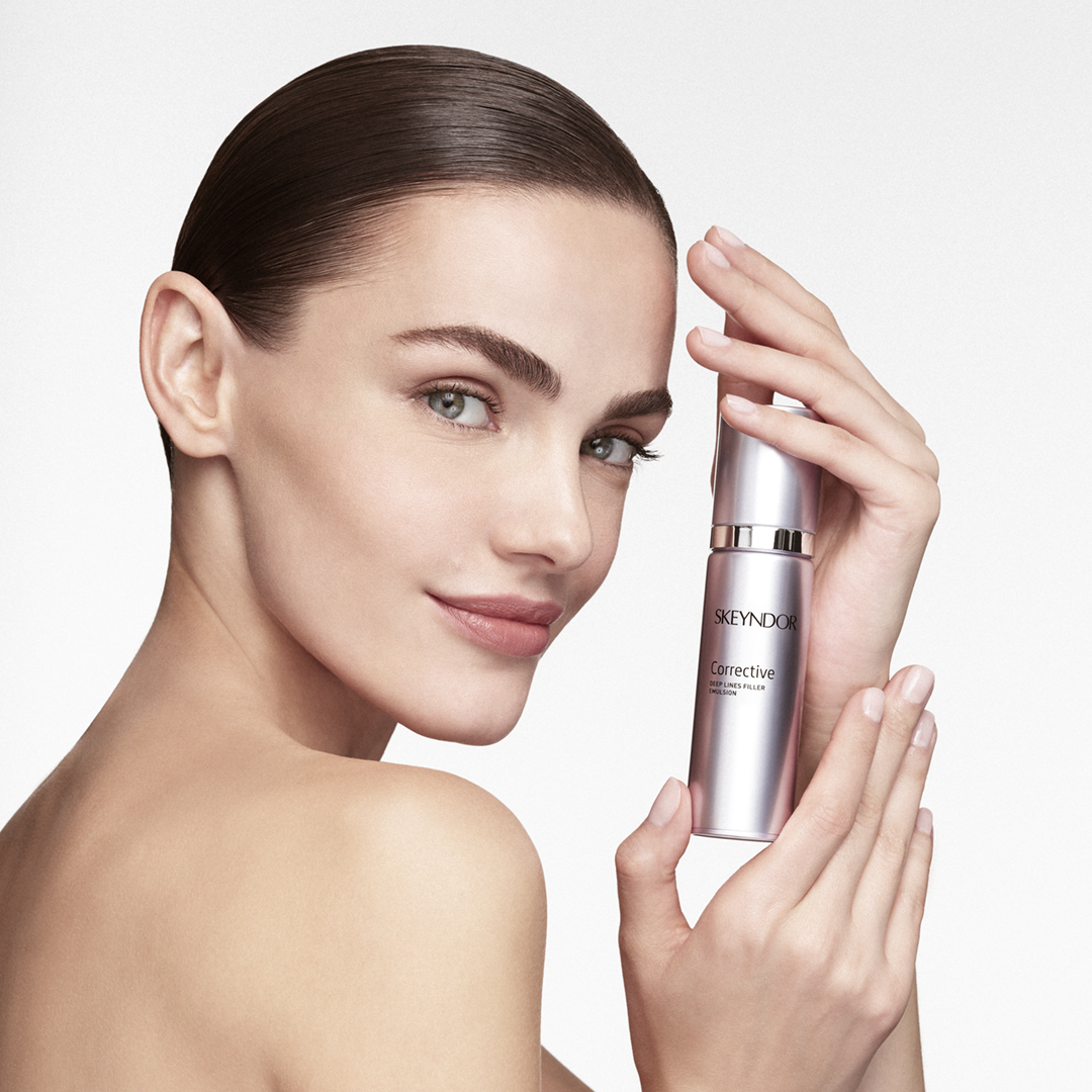Eine Frau, die eine Flasche der Emulsion Skeyndor Corrective Deep Lines Filler in der Hand hält.