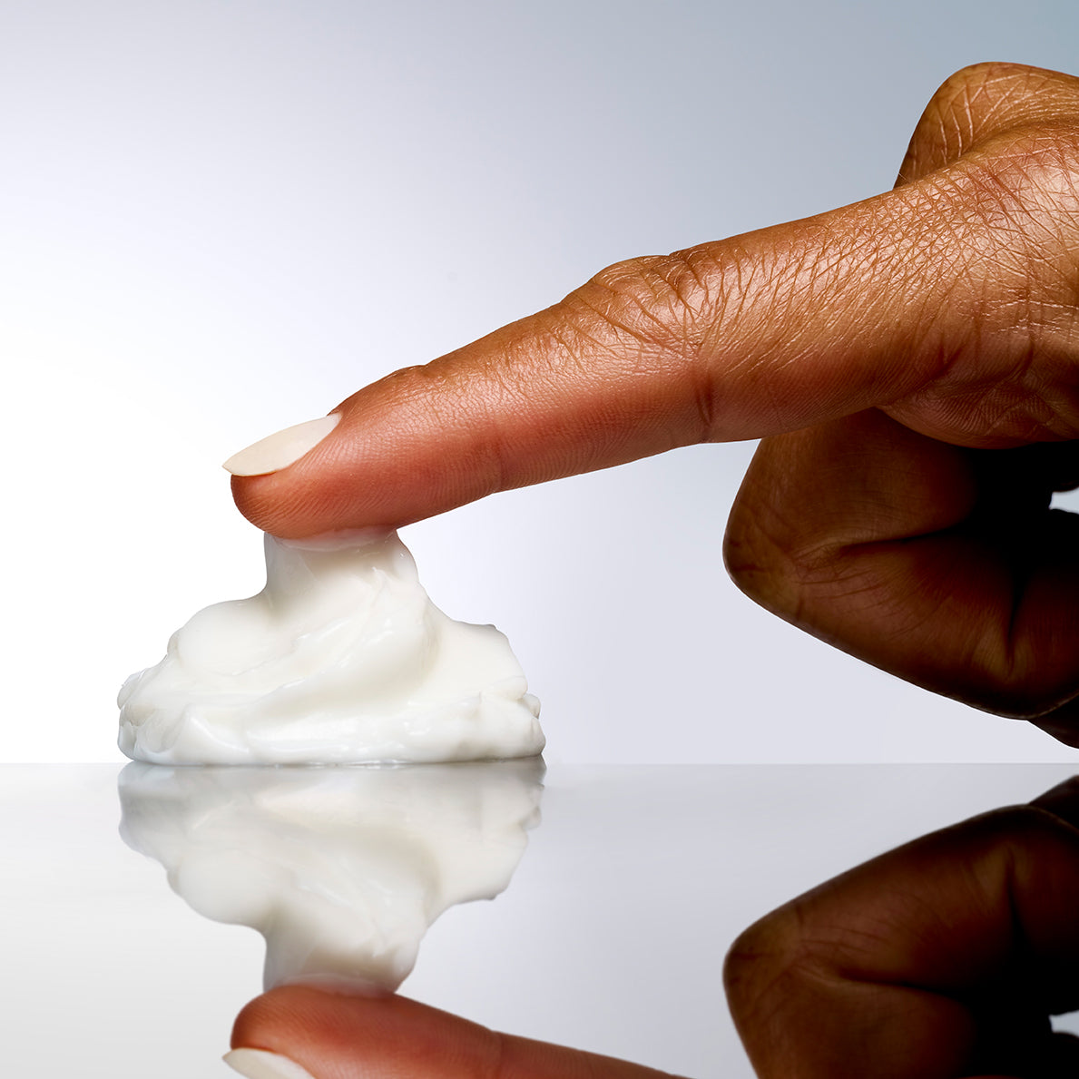 Ein Finger drückt in einen Klecks NeoStrata Restore – PHA Barrier Recovery Cream auf einer spiegelnden Oberfläche – ein Symbol für feuchtigkeitsspendende Pflege für empfindliche Haut.