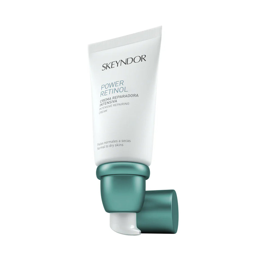 Eine weiße und blaugrüne Tube Skeyndor POWER RETINOL INTENSIVE REPAIRING CREAM ist aufrecht abgebildet, wobei die blaugrüne Kappe entfernt wurde und auf dem Boden liegt.