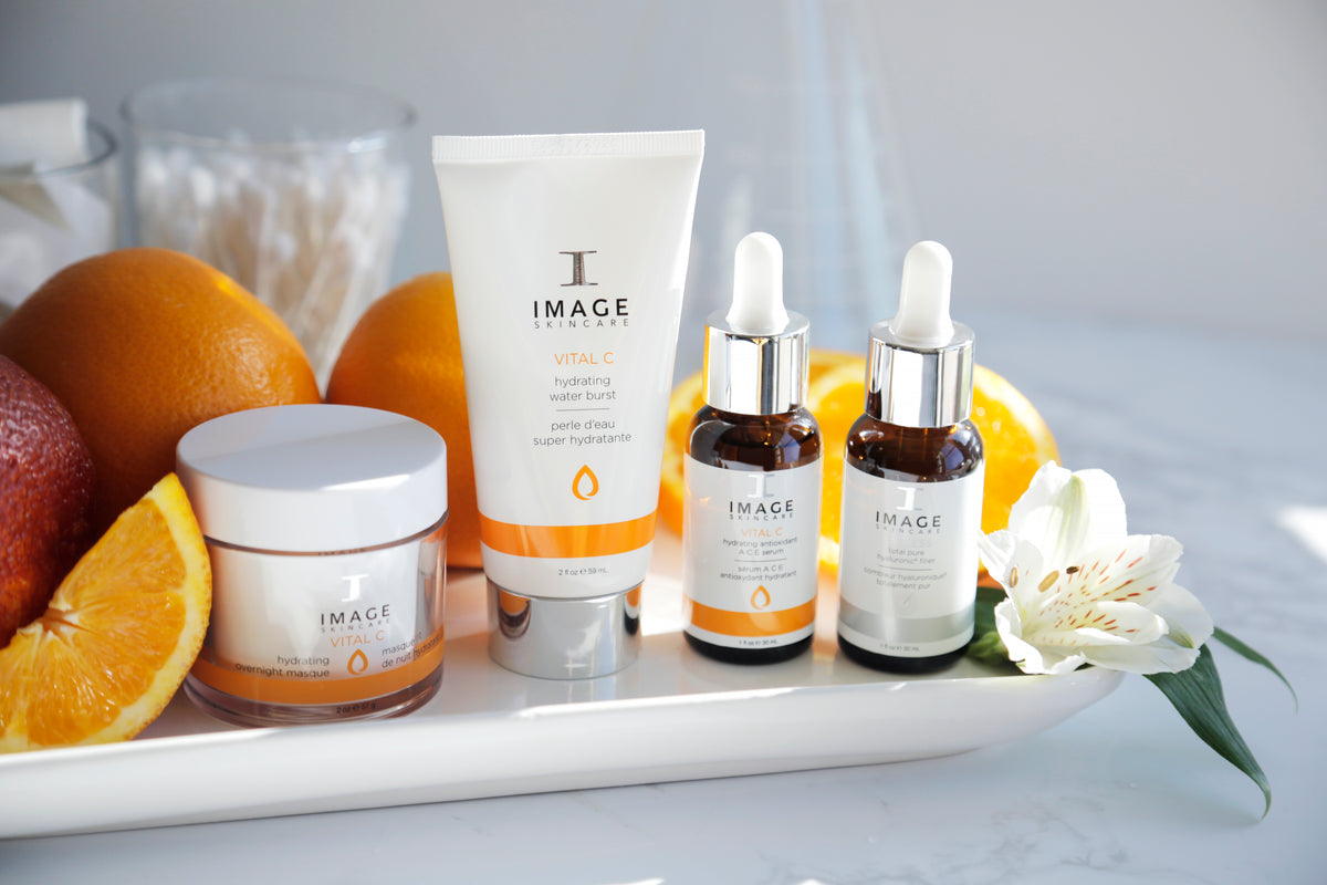 Vier Produkte der Marke Image Skincare Vital C, angeordnet auf einem Tablett mit Orangenscheiben und einer weißen Blume.